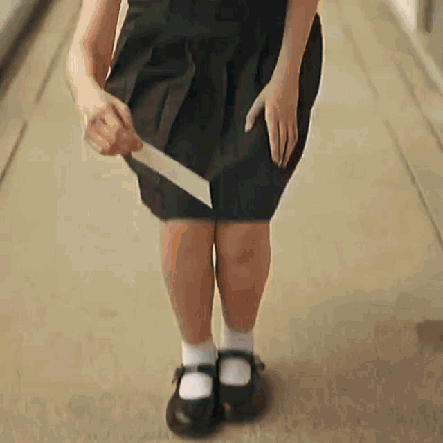 a girl in a black skirt is holding a knife in her skirt .