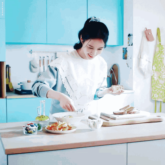 a woman in a white apron is preparing food in a kitchen with blue cabinets ..