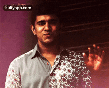 a man in a patterned shirt is waving his hand in front of a wall .