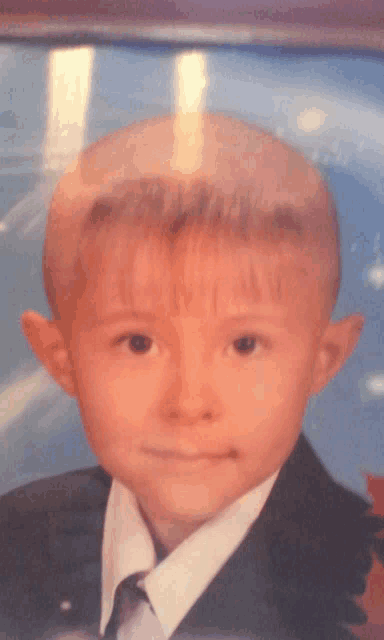 a young boy is wearing a suit and tie and looking at the camera