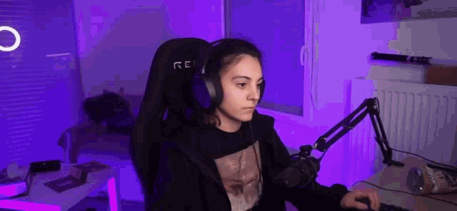a woman is sitting in a gaming chair wearing headphones and using a computer .