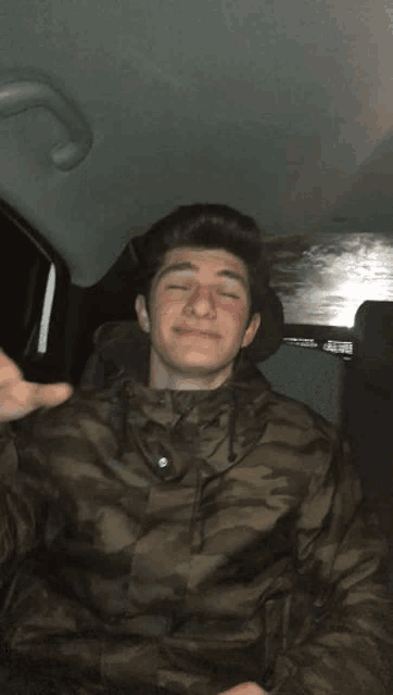a young man wearing a camouflage jacket is sitting in the back seat of a car