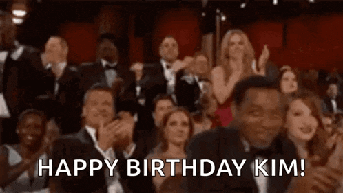 a crowd of people are sitting in a theater and applauding while a man says `` happy birthday kim '' .