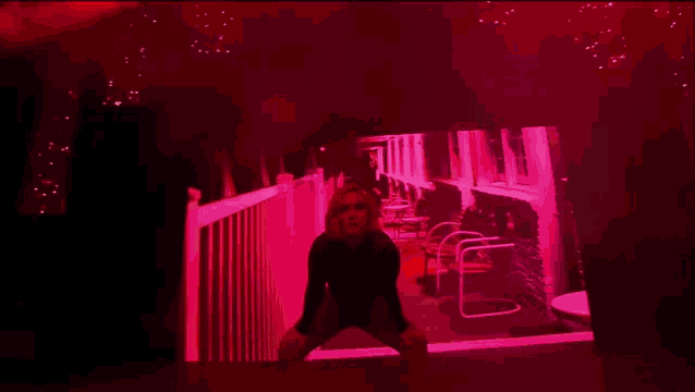 a woman is standing on a balcony in a dark room with red lights behind her