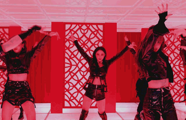 a group of young women are dancing in front of a red wall