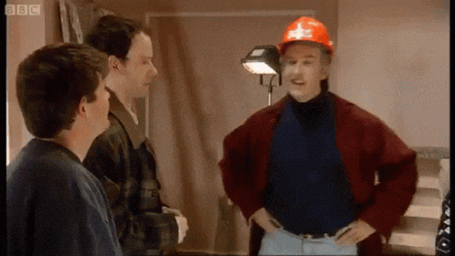 a man wearing a red hard hat is standing in a room with two other men .