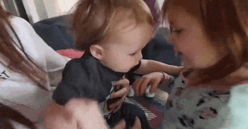 a little girl is holding a baby in her arms and the baby is looking at the girl .