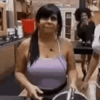 a woman in a purple tank top is standing in a kitchen with other women .
