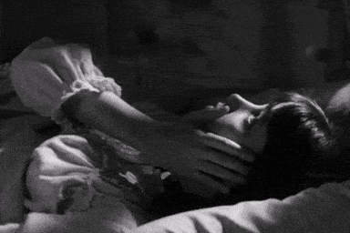 a black and white photo of a woman laying down with her hand on her neck .
