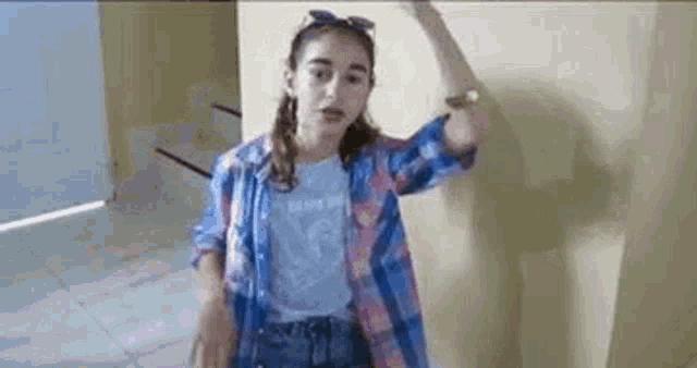 a young girl wearing a plaid shirt and jeans is standing in front of a wall .