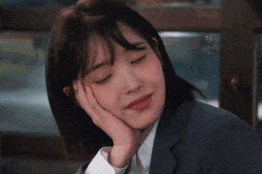 a woman in a suit rests her head on her hand with her eyes closed