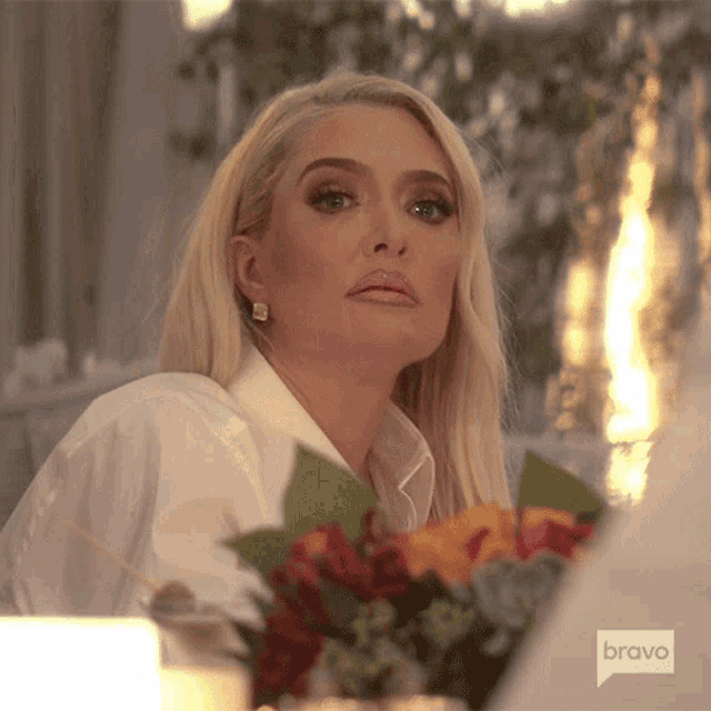 a woman sitting at a table with a bouquet of flowers and a bravo logo on the bottom