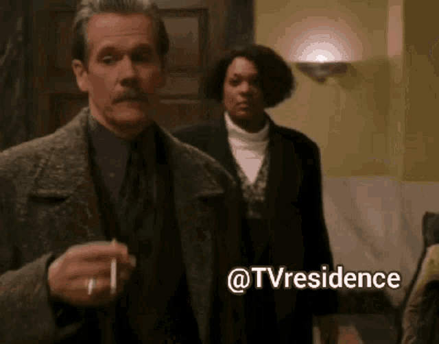 a man with a mustache is smoking a cigarette in front of a woman with the words @tvresidence written on the bottom