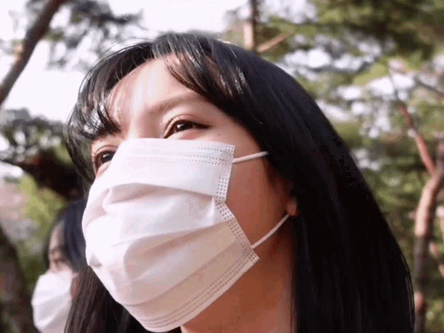 a woman wearing a white face mask looks to the side