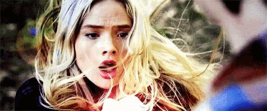 a close up of a woman 's face with her hair blowing in the wind and a man standing behind her .