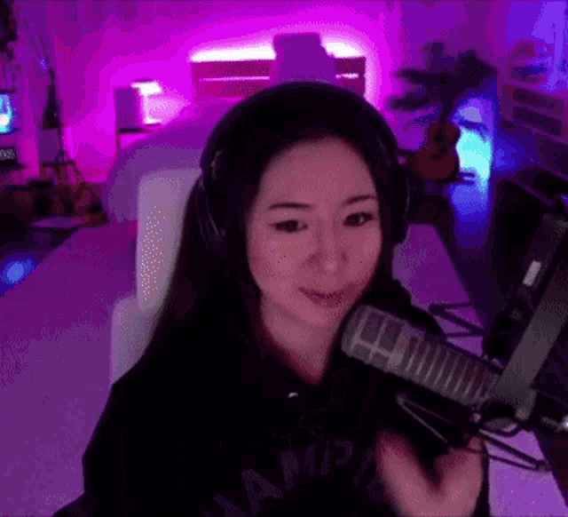 a woman wearing headphones is sitting in front of a microphone in a room with purple lights .