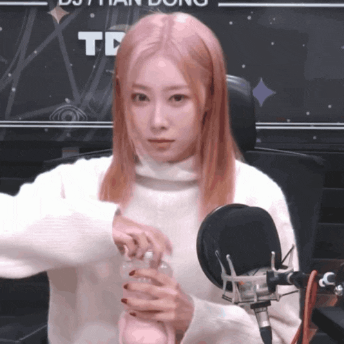 a woman in a white sweater is sitting in front of a microphone holding a drink