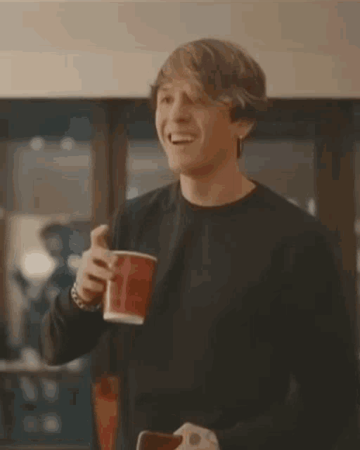 a young man in a black sweater is holding a red cup and smiling .