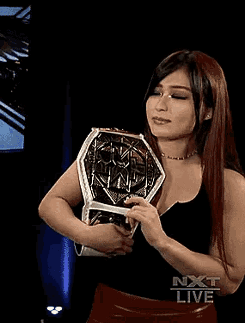 a woman is holding a wrestling championship belt in her hands in a dark room .