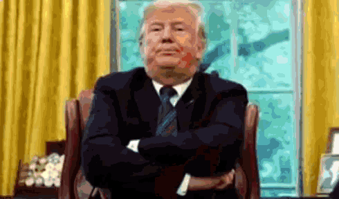a man in a suit and tie is sitting with his arms crossed in front of a window .