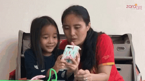 a woman and a little girl are looking at a cell phone together