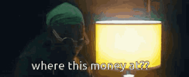 a man in a green hat is talking on a cell phone in front of a lamp .