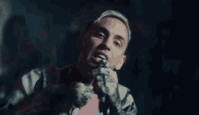 a man with tattoos on his arms is singing into a microphone .