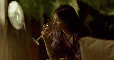 a woman is sitting at a table holding a glass of wine and looking out a window .