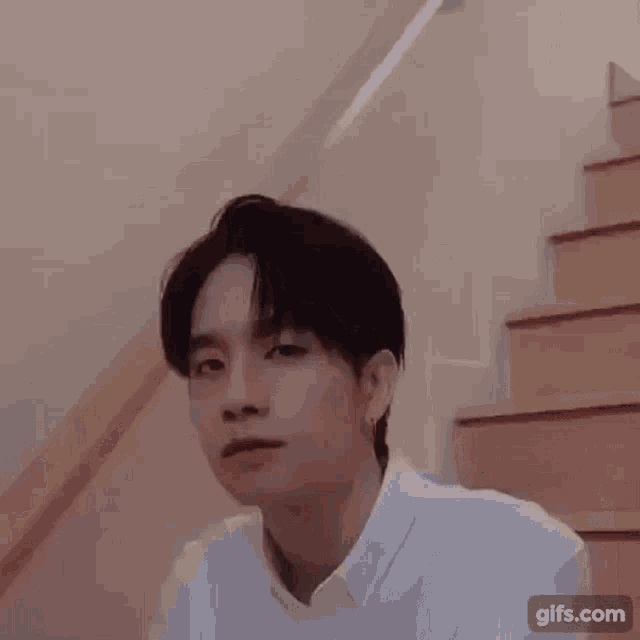 a young man wearing a white shirt and earrings is sitting on a staircase .