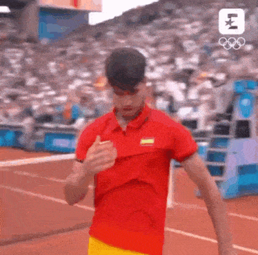 a man wearing a red shirt and yellow shorts is running on a track .
