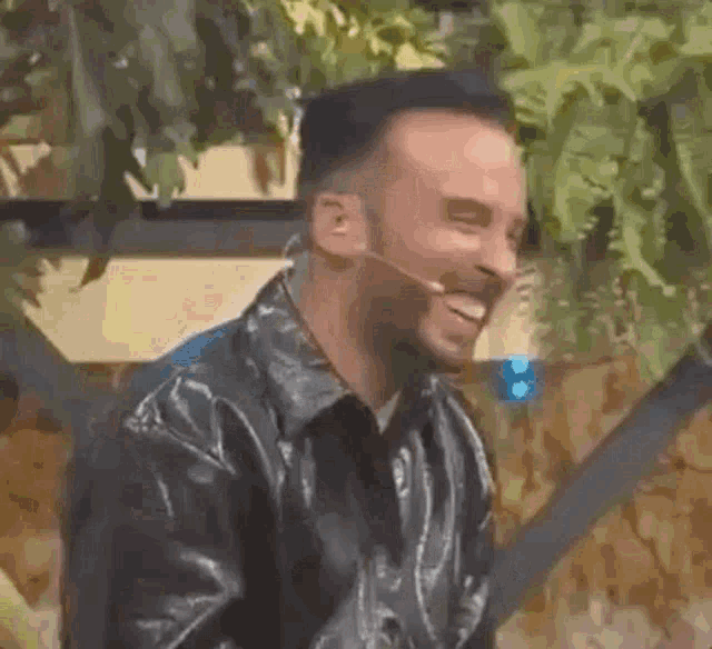 a man in a leather jacket is laughing and wearing a microphone around his neck .