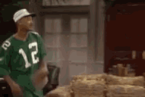 a man wearing a green jersey with the number 12 on it is standing in front of a pile of logs .