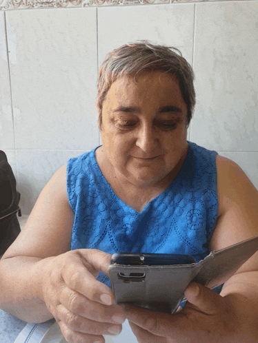 a woman in a blue top is holding a cell phone
