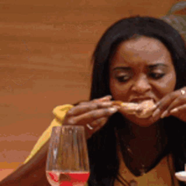 a woman is sitting at a table with a glass of wine and eating a piece of food .