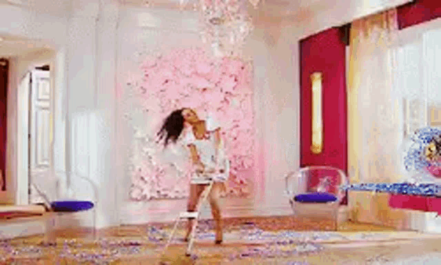 a woman is dancing in a room with a chandelier and confetti on the floor .