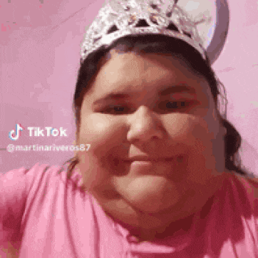a woman wearing a pink shirt and a silver tiara is smiling .