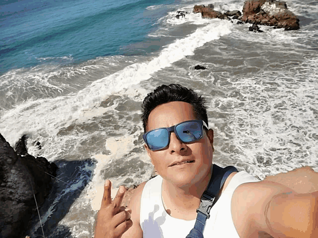a man wearing sunglasses takes a picture of himself on a beach