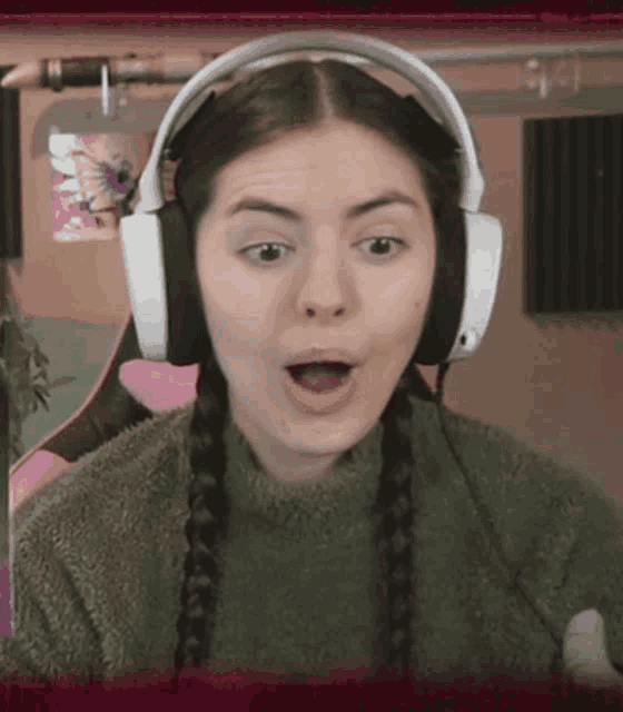 a woman wearing headphones and a green sweater looks surprised