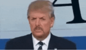 a man in a suit and tie is making a funny face while standing in front of an airplane .