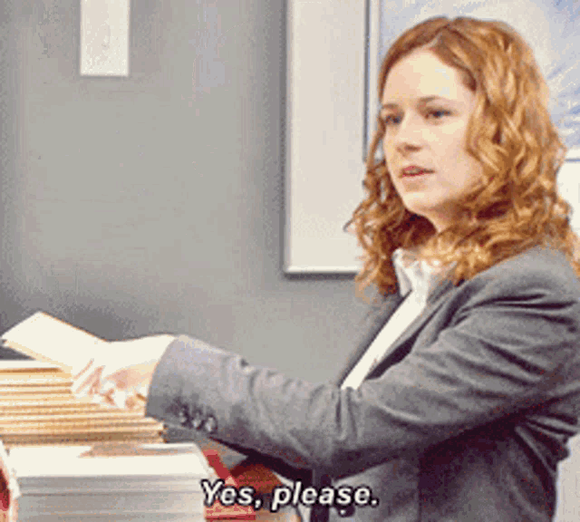 a woman in a suit says yes please in front of a pile of books