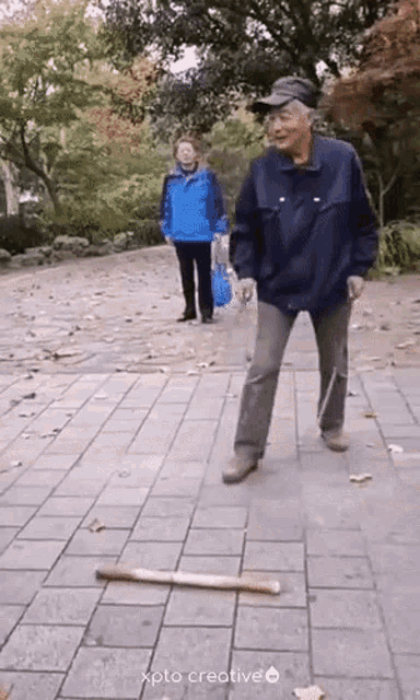 an elderly man with a cane is standing on a brick sidewalk holding a baseball bat .