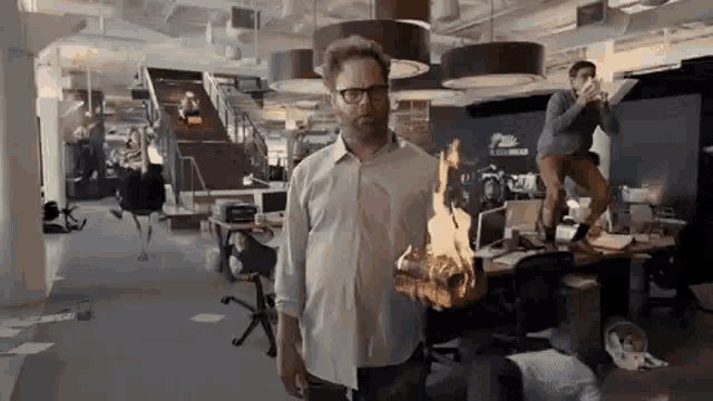 a man in a white shirt is standing in an office with a fireball coming out of his shirt .