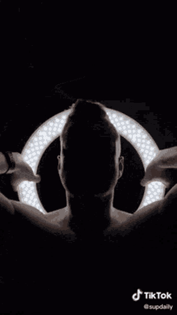 a shirtless man is holding a ring light in front of his head