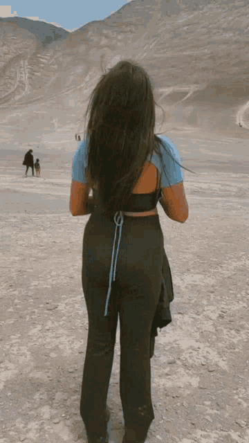 a woman in black pants and a blue shirt stands in the desert
