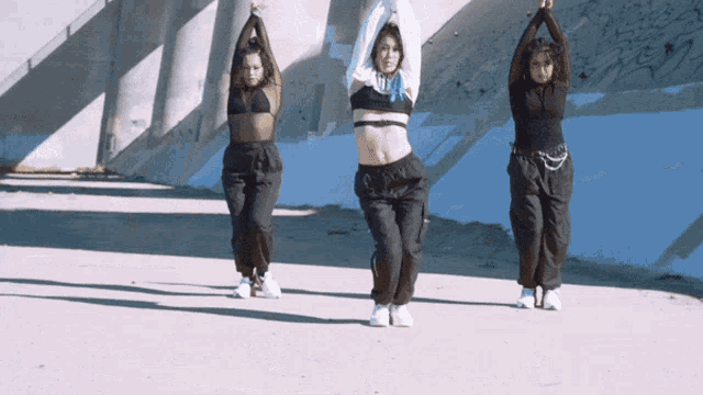 three women are dancing in front of a blue wall with their arms up in the air