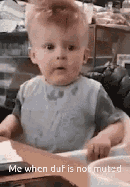 a baby is sitting at a table with the words me when duf is not muted