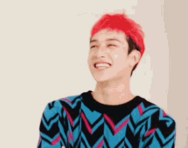 a man with red hair is wearing a blue and black sweater and smiling