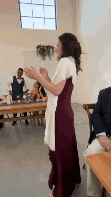 a woman in a burgundy dress is clapping at a wedding