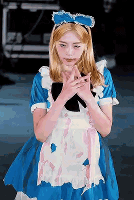 a woman dressed as alice in wonderland holds her hands together in front of her face