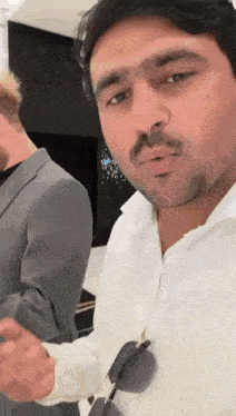 a man wearing sunglasses and a white shirt looks at the camera